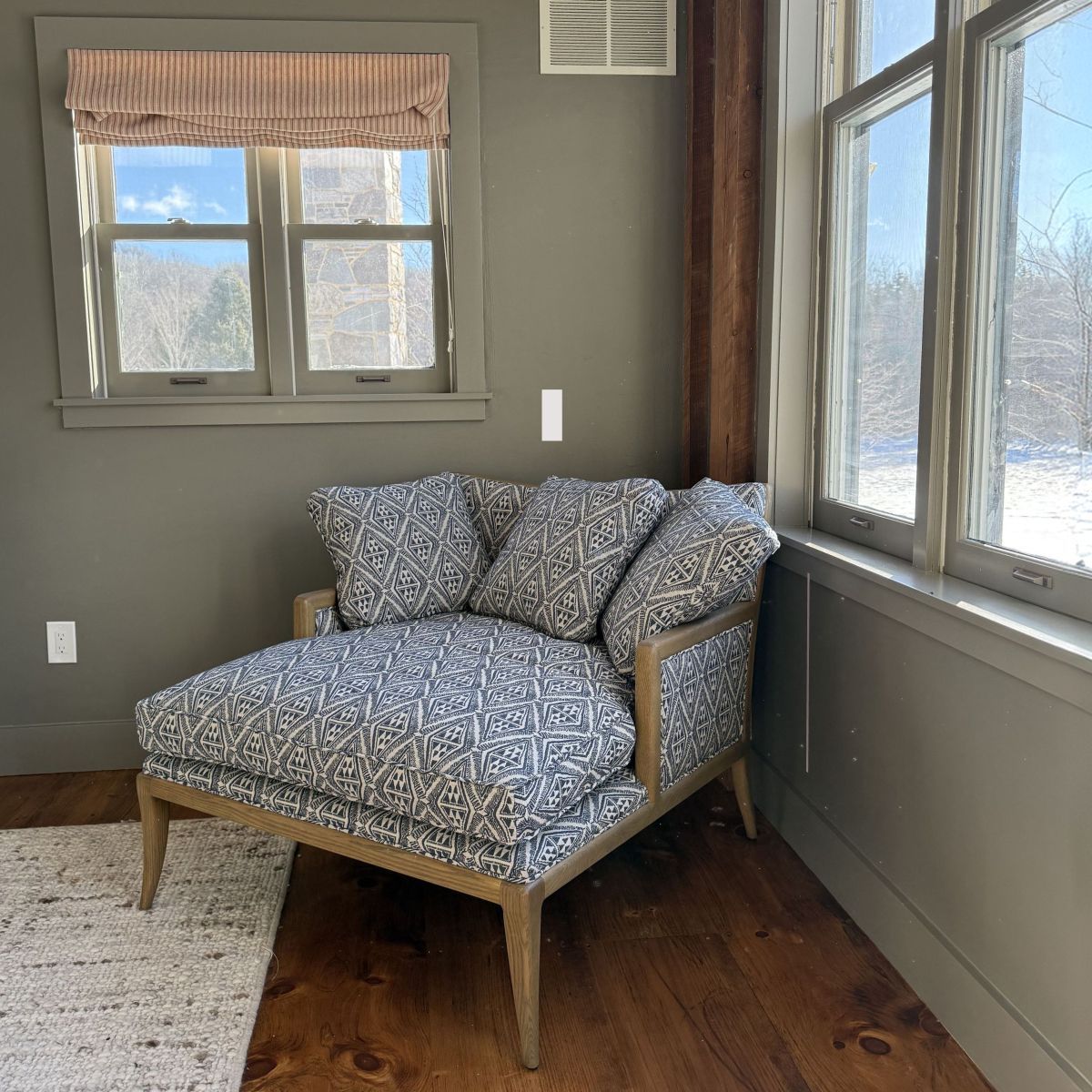 Cozy corner chair with patterned cushions in a sunlit room with windows and wood floors