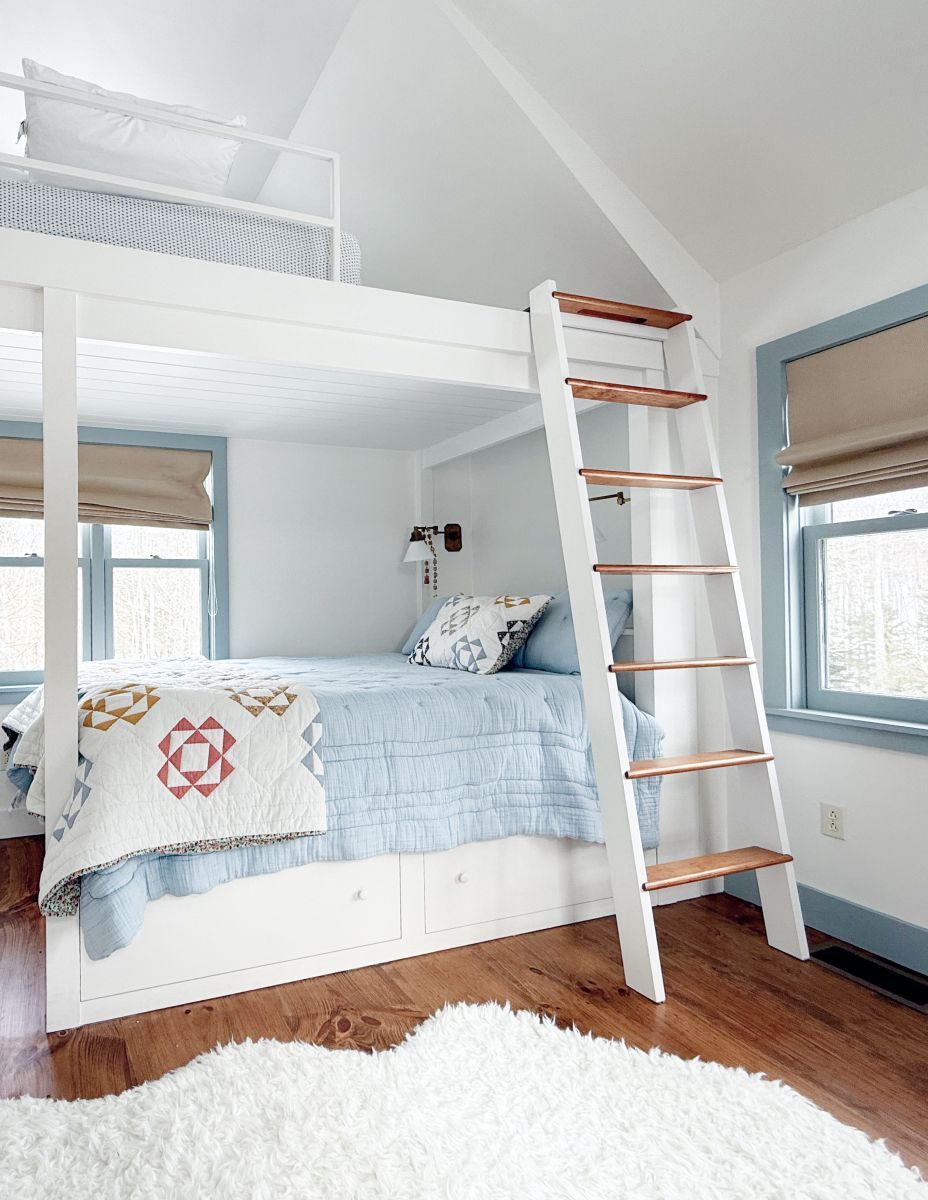 Bright bedroom with white loft bed, ladder, blue bedding, and windows with blinds
