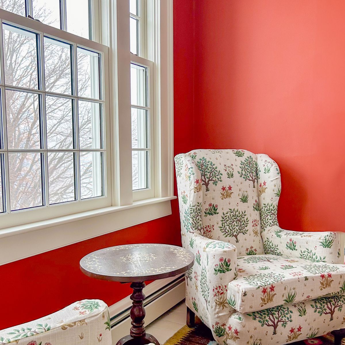 Floral armchair and small round table beside a bright window in a red-walled room