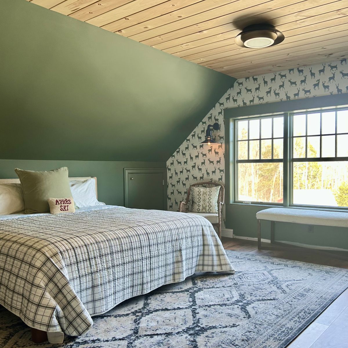 Cozy attic bedroom with sloped ceiling, patterned bedding, green walls, and a large window bench.