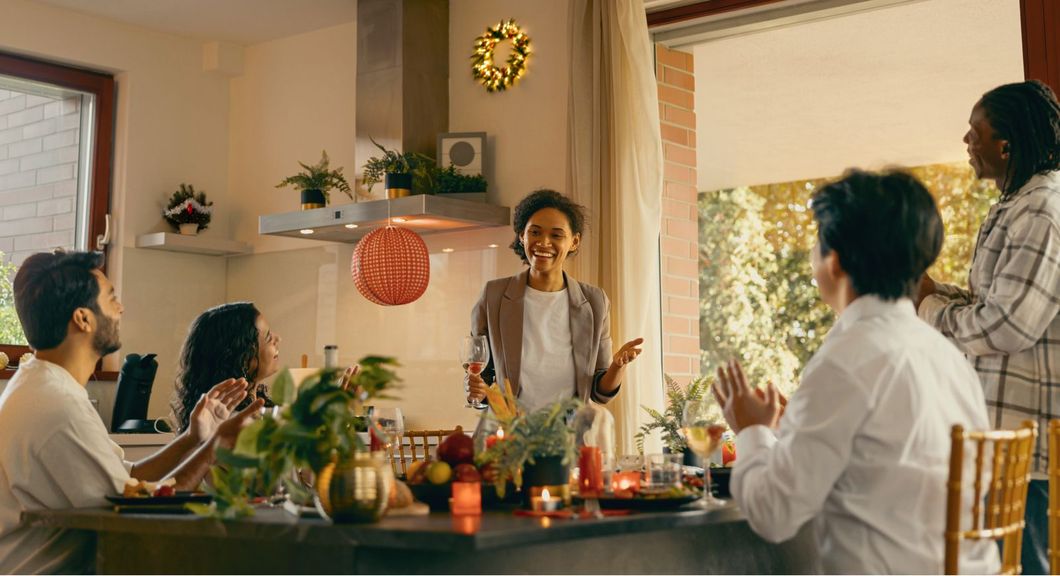 Friends gathered around a decorated dining table for a warm indoor meal, with candles and string lights.