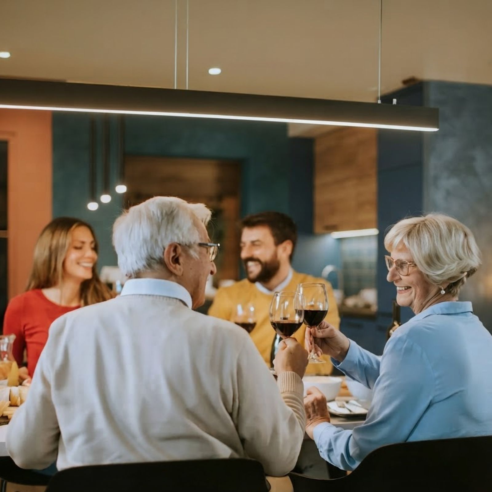 Friends clink wine glasses around a dining table in a warmly lit restaurant.