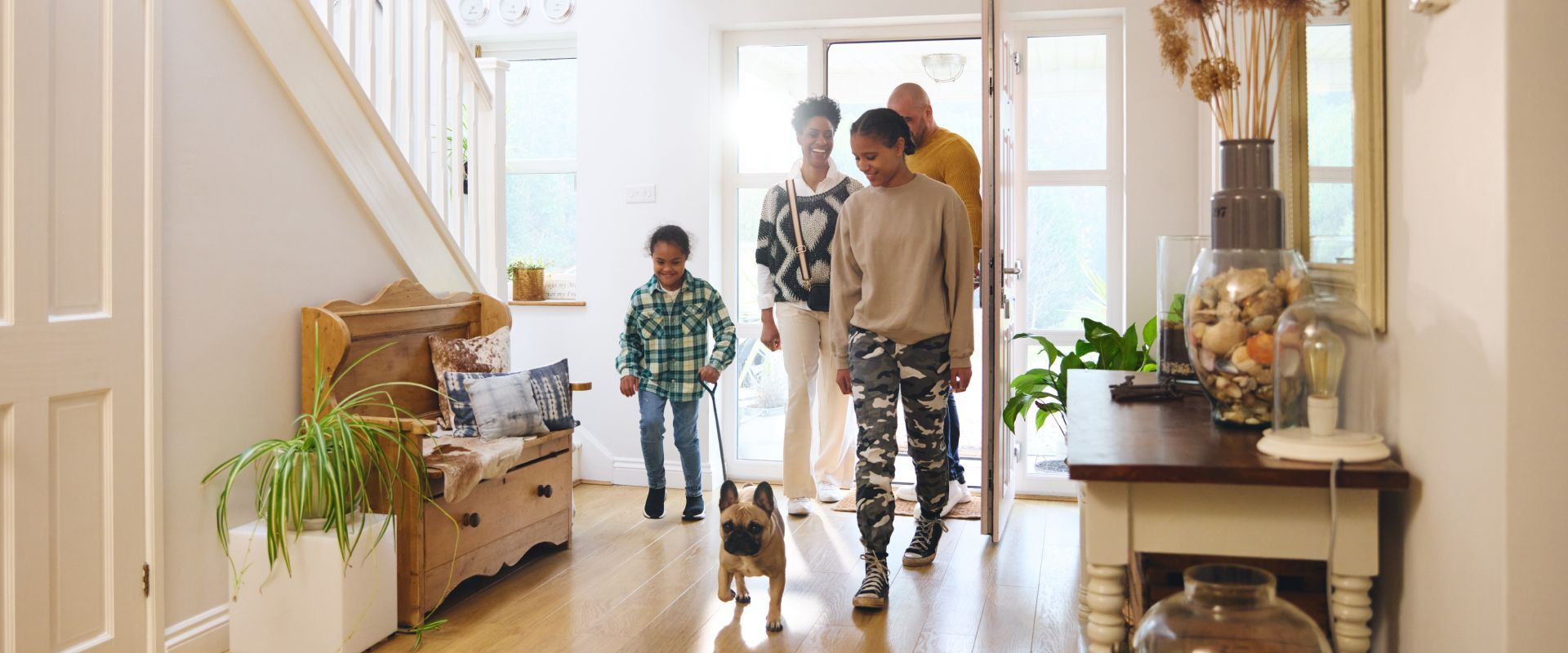 Family walking through a bright entryway with a child, plants, and a staircase