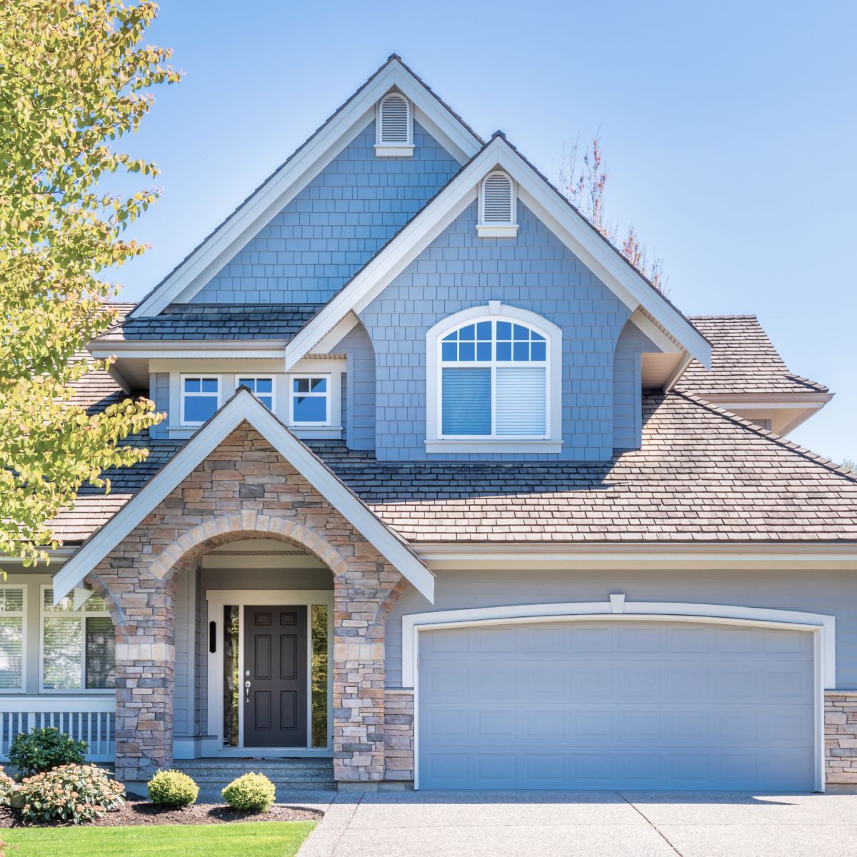 Blue two-story house with stone front, white trim, and double garage under a clear sky