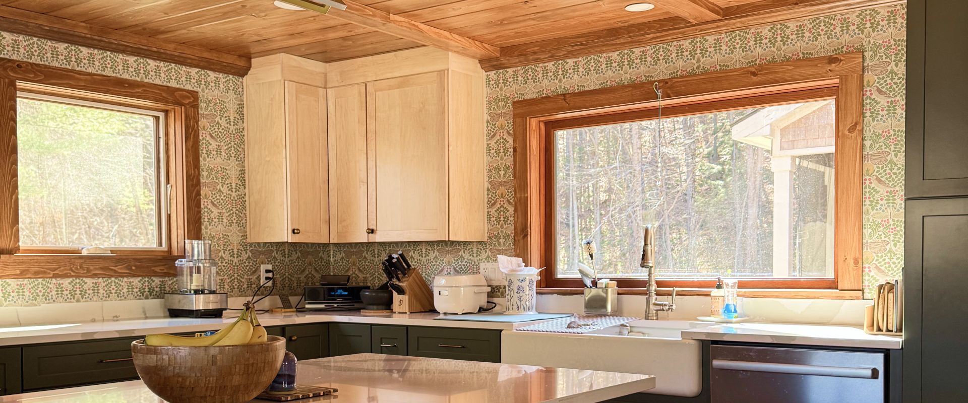 Bright kitchen with light wood cabinets, large windows, and a granite island with bowls and dishes.