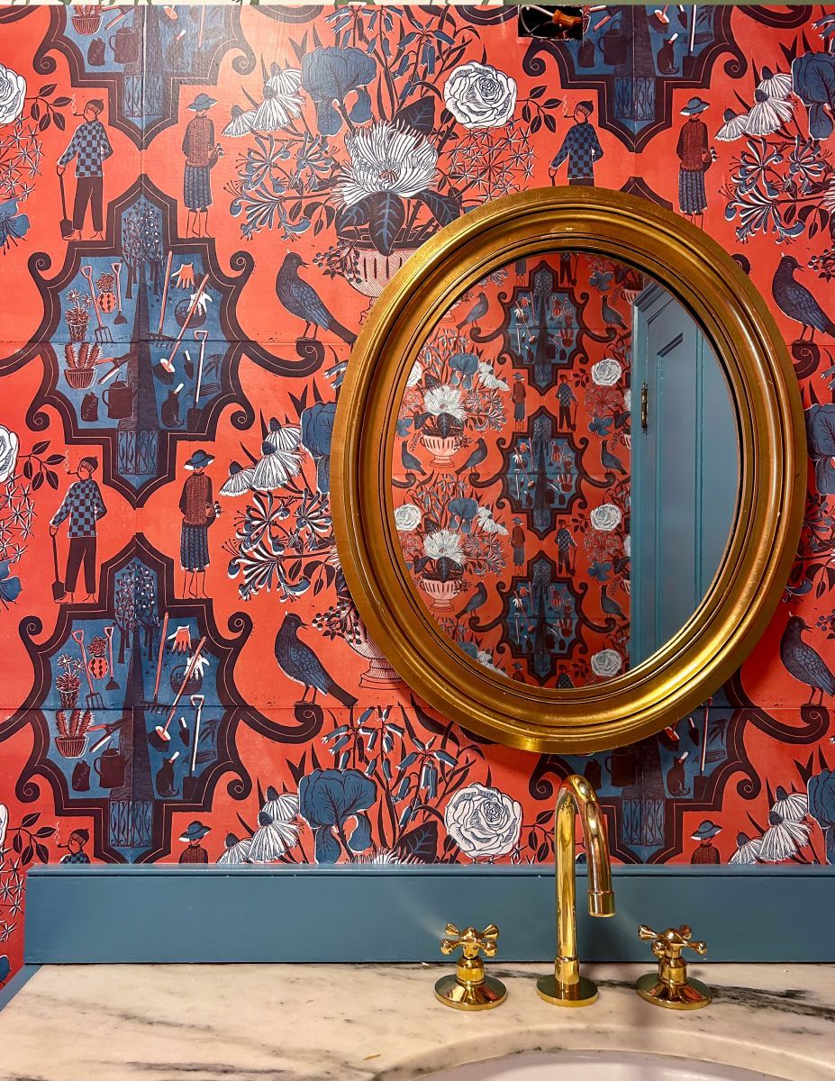 Gold oval mirror above a sink against red patterned wallpaper with blue accents