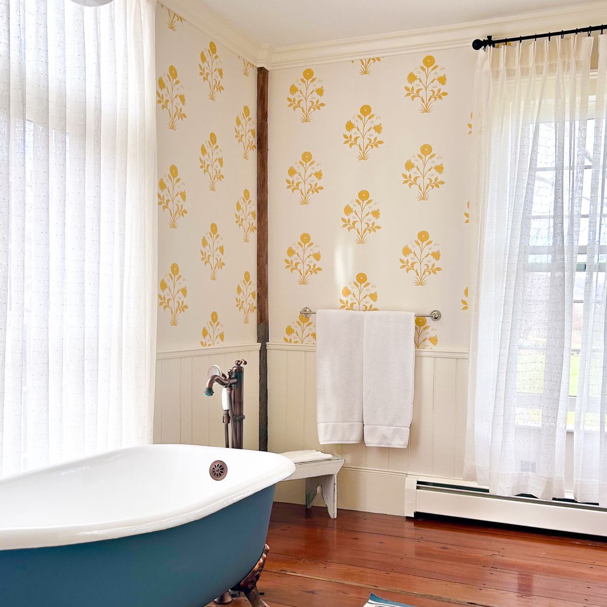 Bright bathroom with clawfoot tub, floral wallpaper, and sheer curtains by a window