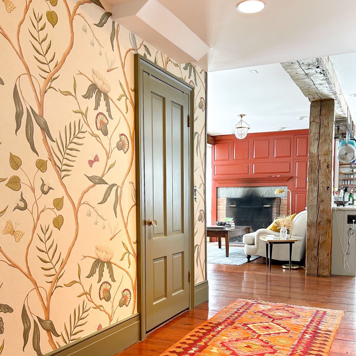 Floral wallpapered hallway with a green door leading to a bright room with red walls, fireplace, and patterned rug