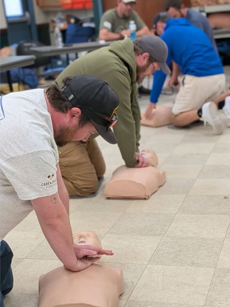 People kneeling on gym floor practicing CPR compressions on mannequins