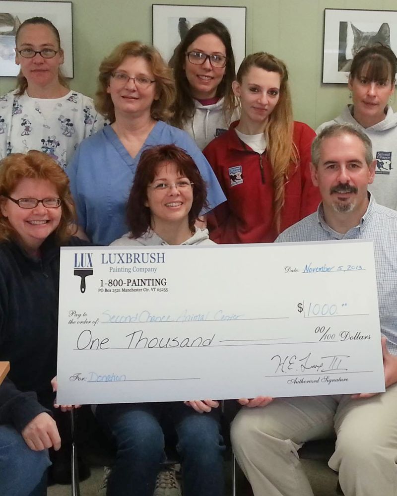 Group holding oversized check for $1,000 in front of a white wall, smiling for a photo