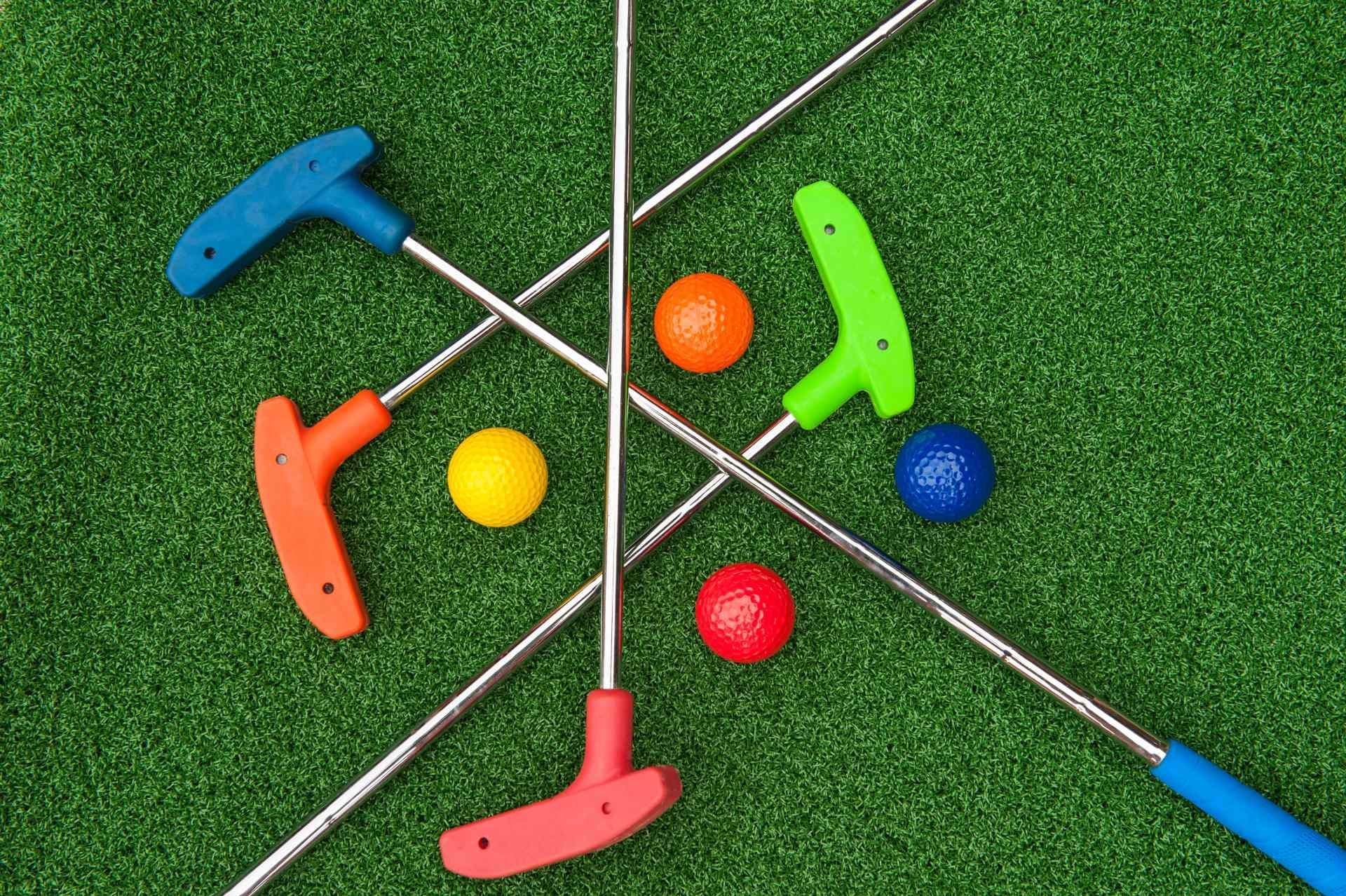 A group of mini golf clubs and balls on a green field.