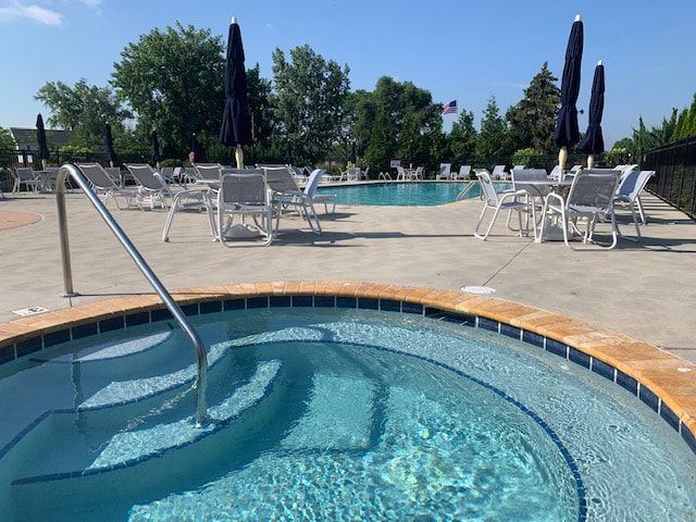 A hot tub surrounded by chairs and umbrellas next to a large swimming pool.