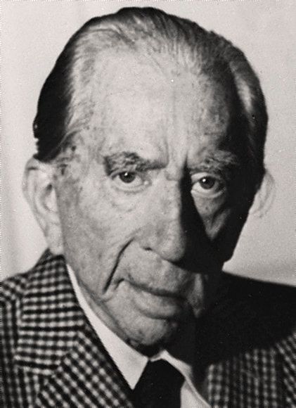 A black and white photo of an older man in a suit and tie