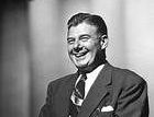 A man in a suit and tie is smiling in a black and white photo.