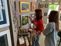 Two women are looking at paintings on a wall in a gallery.