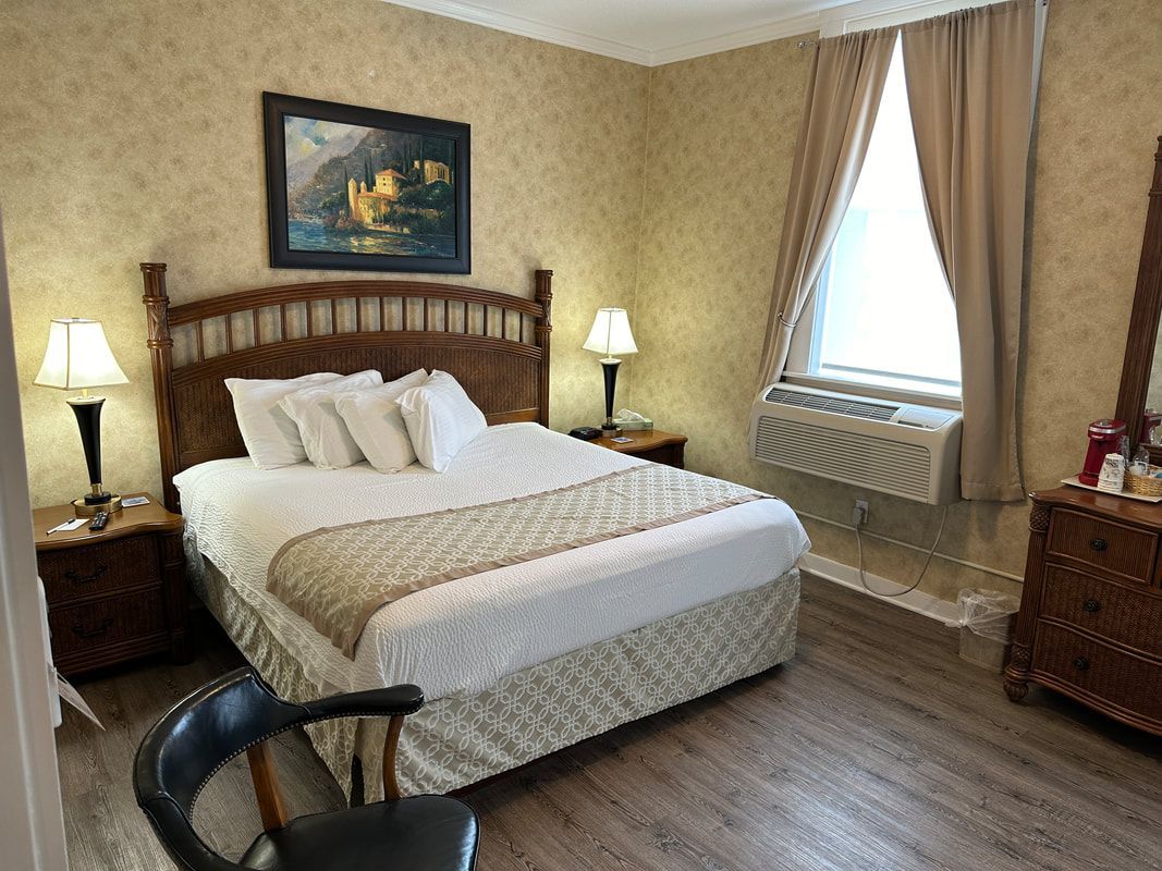 A hotel room with a king size bed , dresser , chair , lamps and a window.
