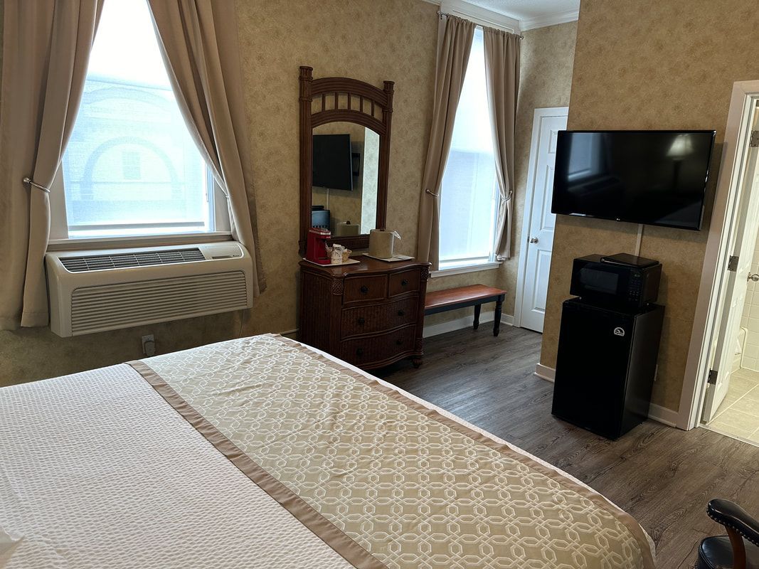 A hotel room with a bed , dresser , television and mirror.