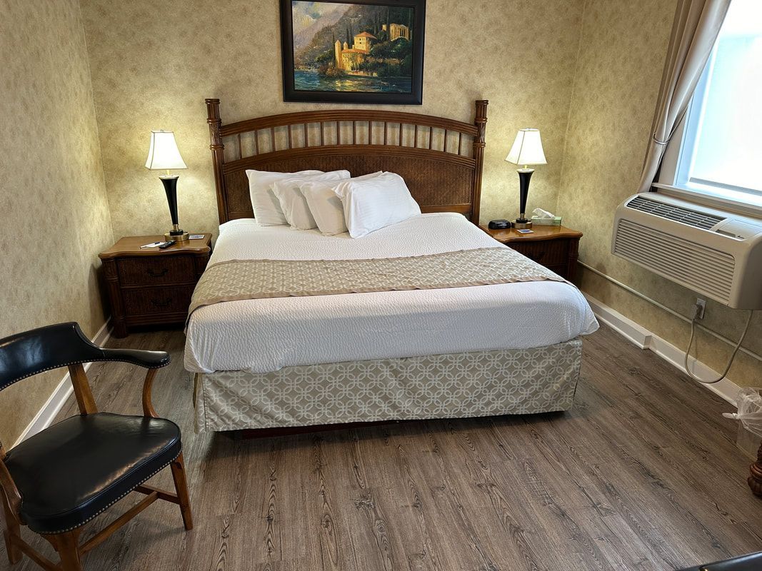 A hotel room with a bed , chair , lamps and a window.