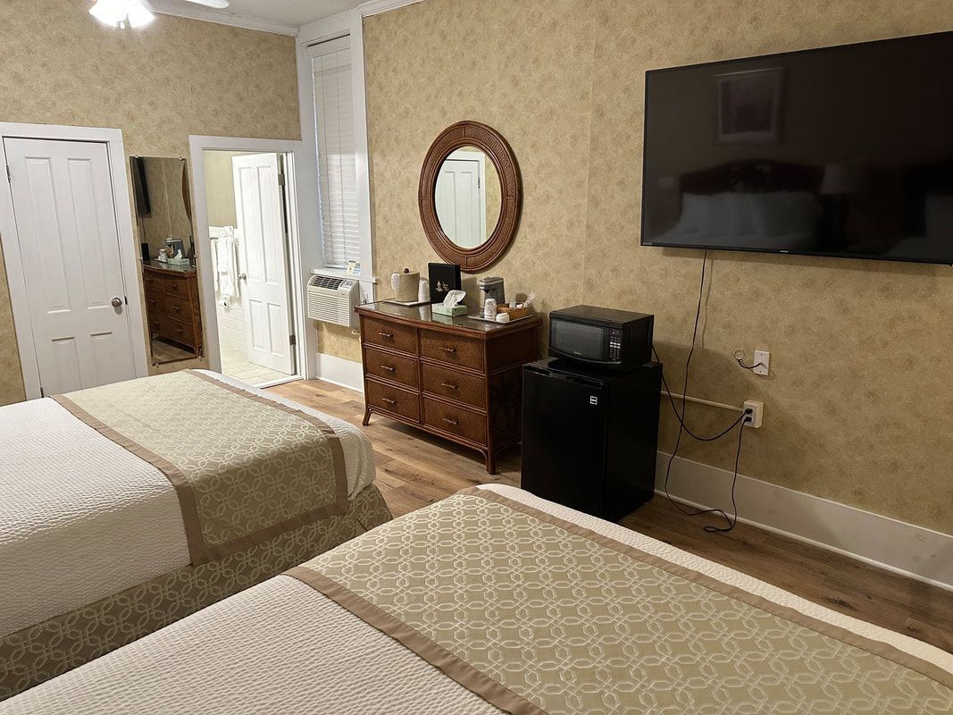 A hotel room with two beds , a dresser , a microwave , and a flat screen tv.
