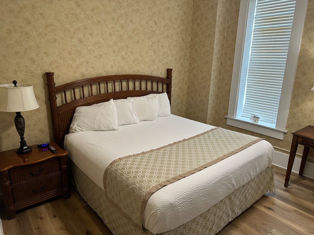 A bedroom with a bed , nightstand , lamp and window.