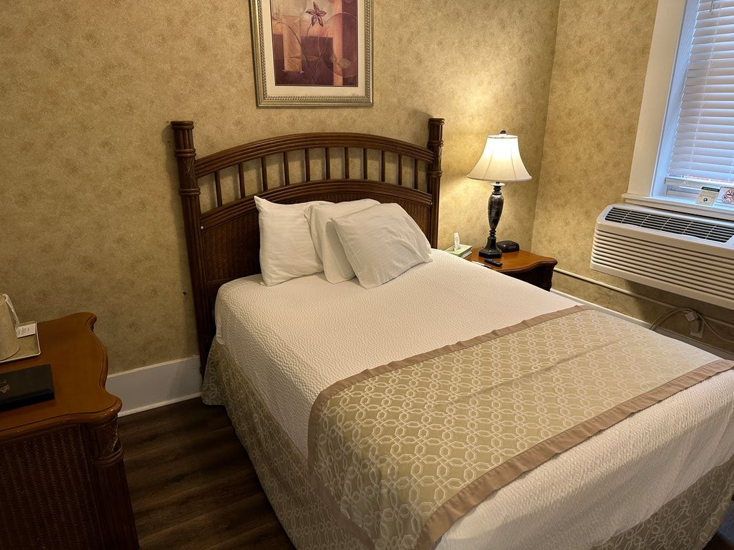 A hotel room with a bed , nightstand , lamp and window.