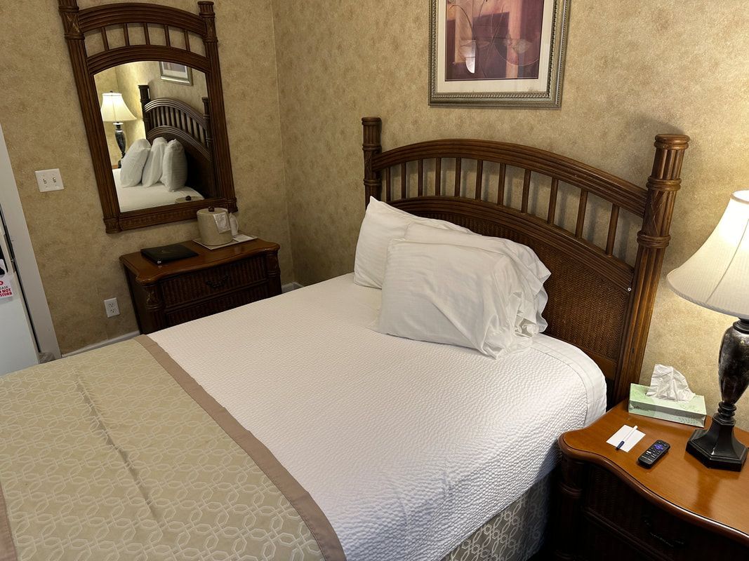 A hotel room with a bed , nightstand , lamp and mirror.