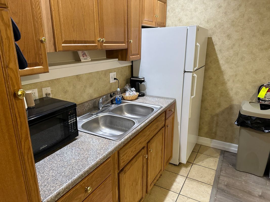 A kitchen with a sink , refrigerator , microwave and trash can.