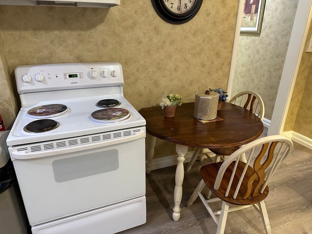 A kitchen with a stove , table and chairs and a clock on the wall.