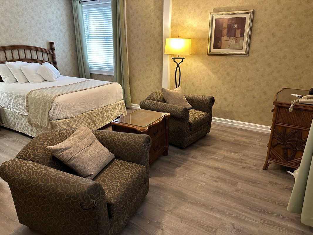A bedroom with a bed , two chairs , a table and a lamp.