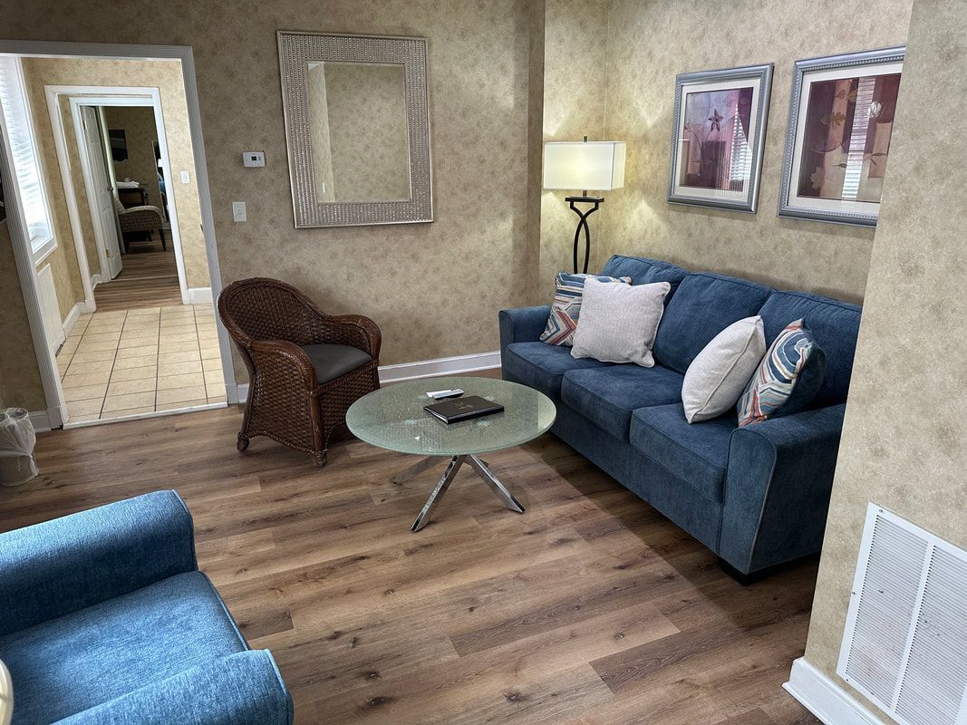 A living room with a blue couch , chair , coffee table and mirror.