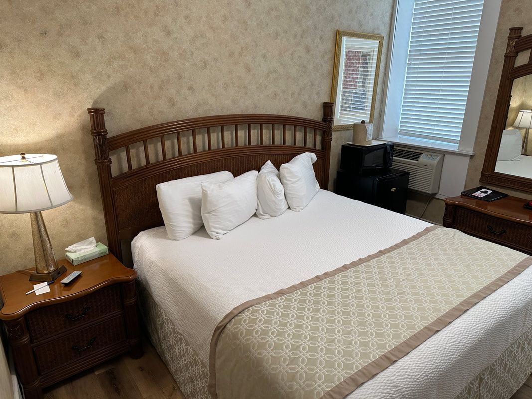 A hotel room with a bed , nightstand , lamp and mirror.