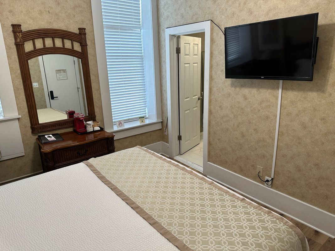 A bedroom with a bed , dresser , mirror and flat screen tv.
