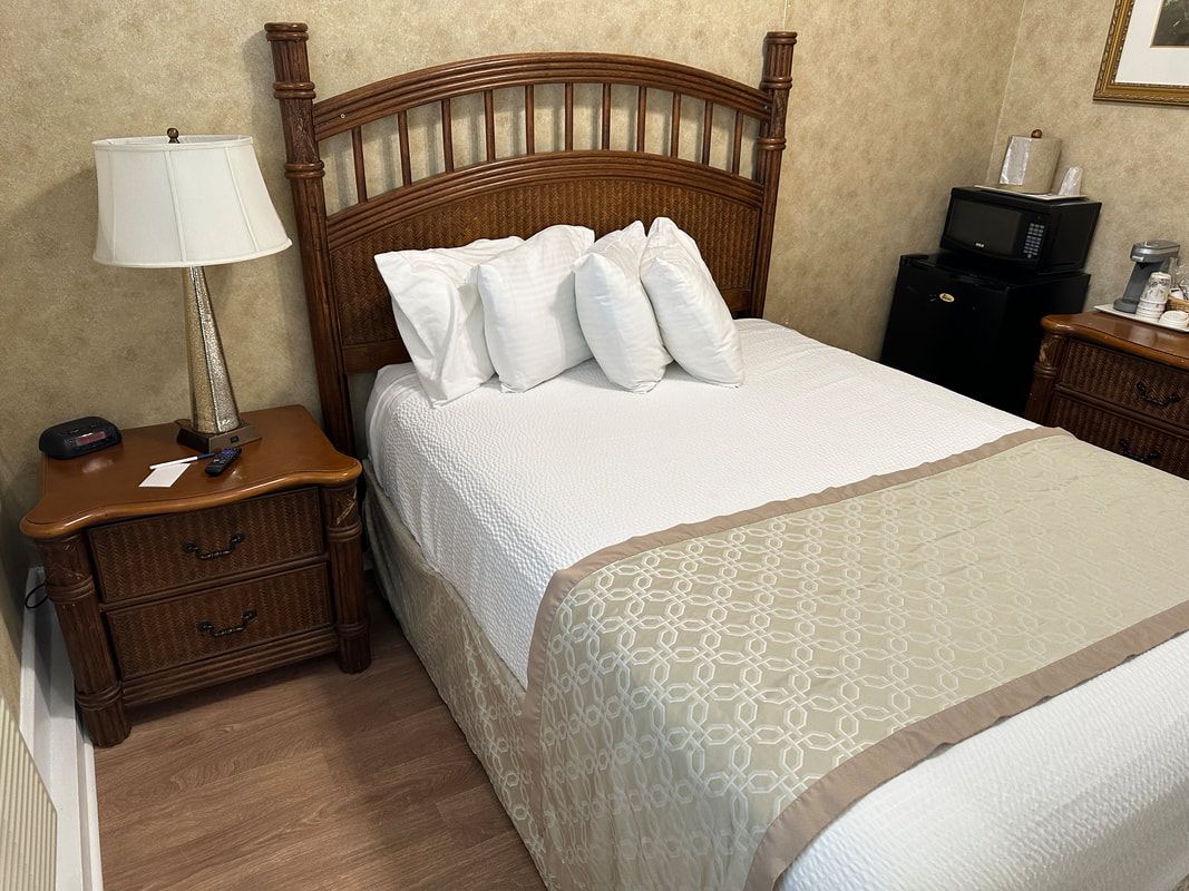 A hotel room with a bed , nightstand , lamp and microwave.