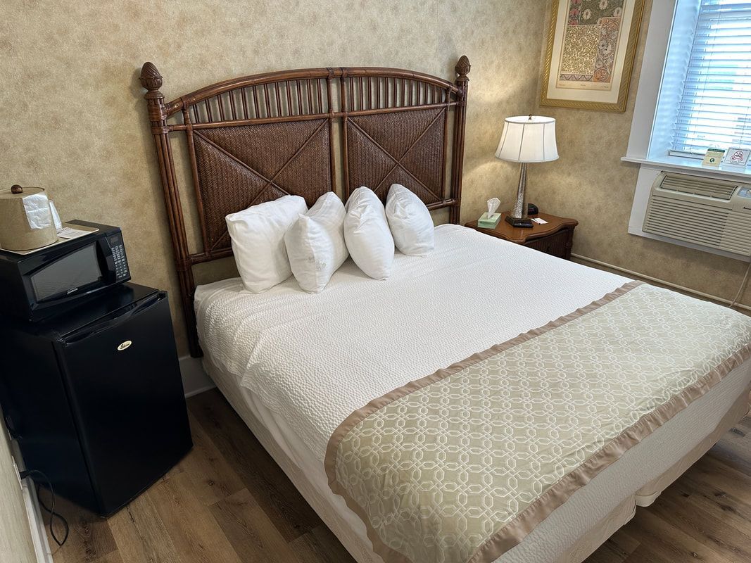 A hotel room with a bed , refrigerator , microwave and lamp.