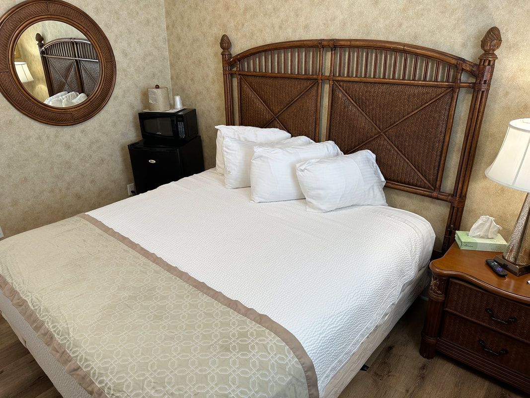 A hotel room with a bed , nightstand , lamp and mirror.