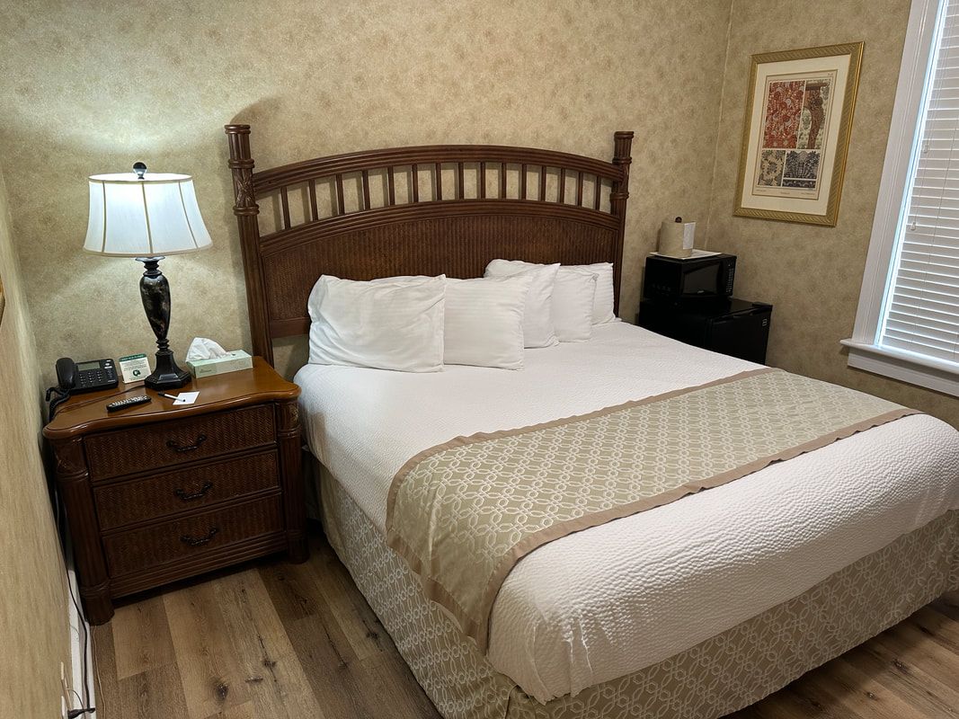 A hotel room with a bed , nightstand , lamp and window.