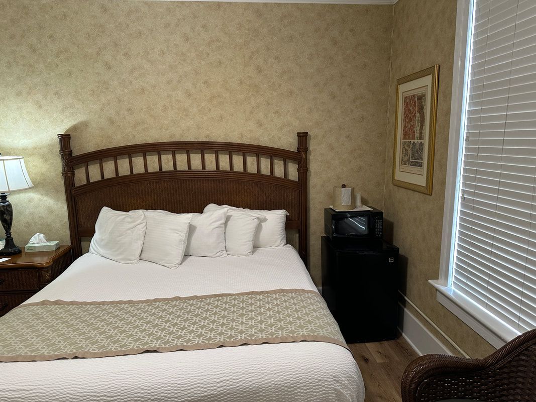 A bedroom with a bed , chair , nightstand , microwave and window.