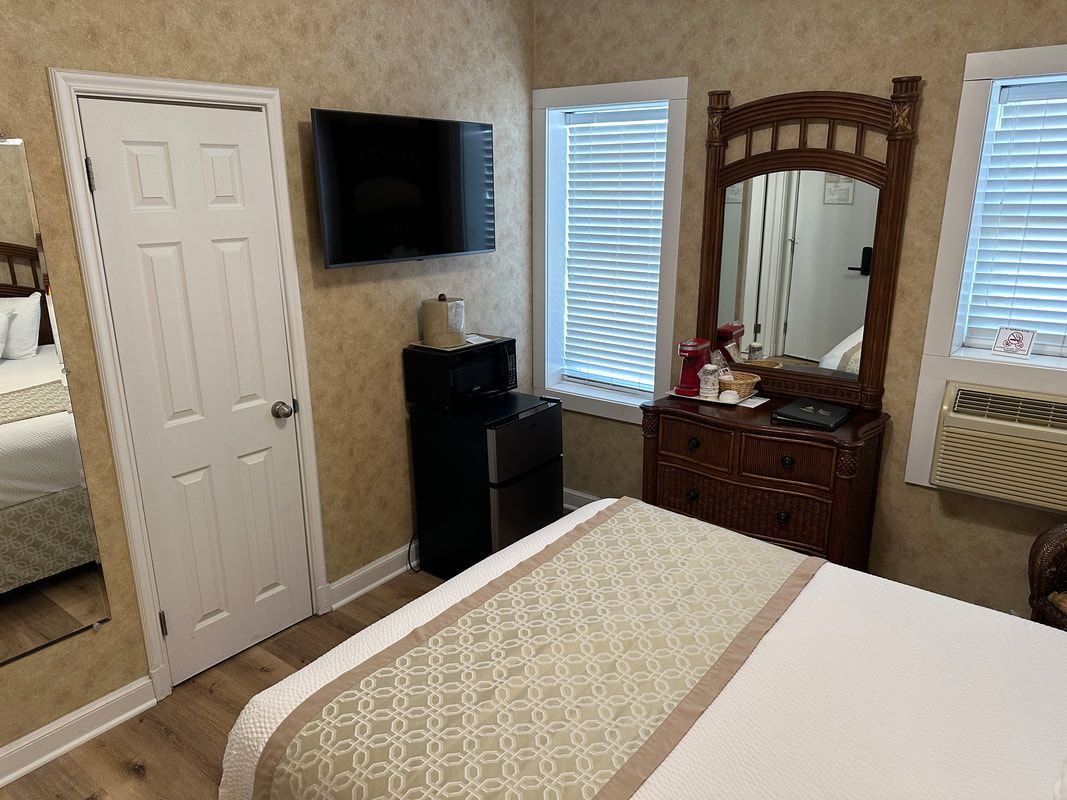 A hotel room with a bed , television , mirror and dresser.