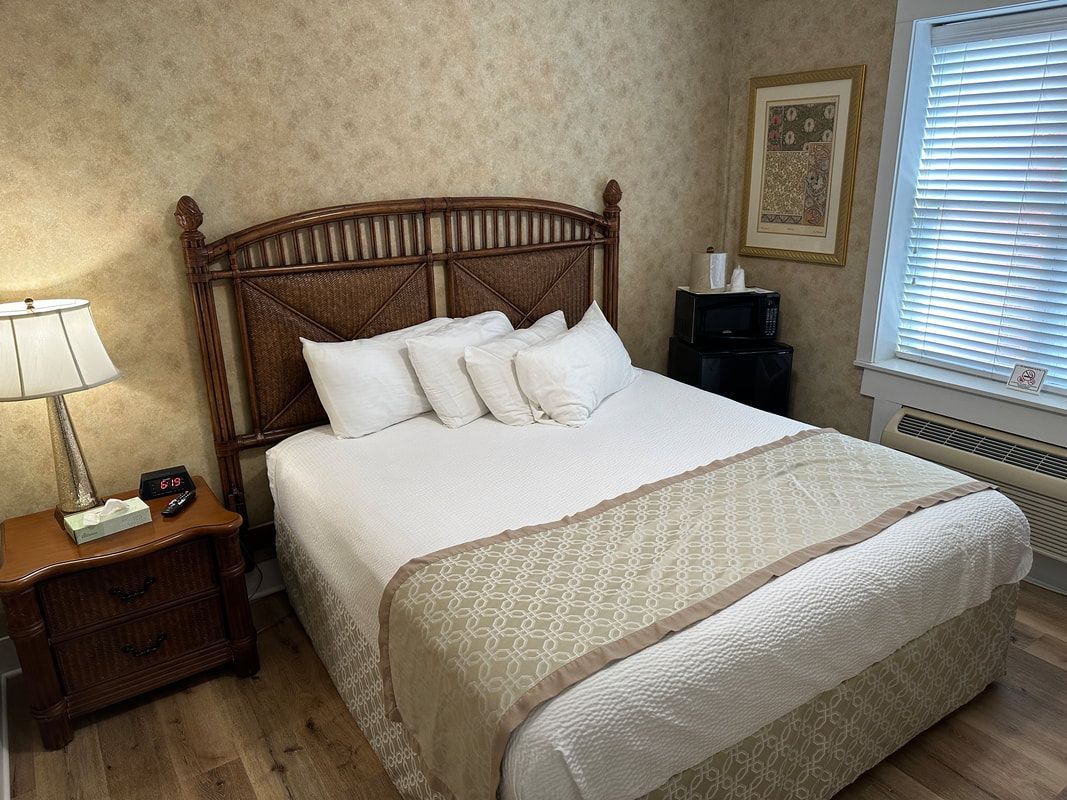 A bedroom with a bed , nightstand , lamp and window.