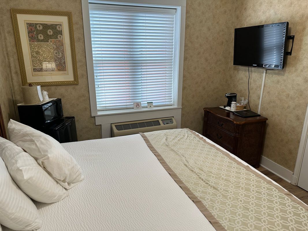 A hotel room with a bed , dresser , television and window.