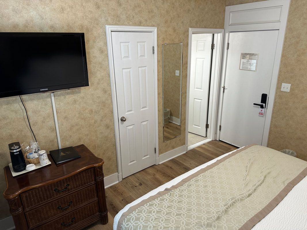 A hotel room with a bed , dresser , television and mirror.