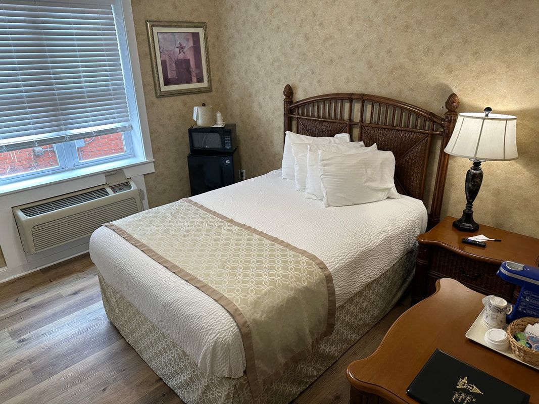 A hotel room with a bed , nightstand , lamp and window.