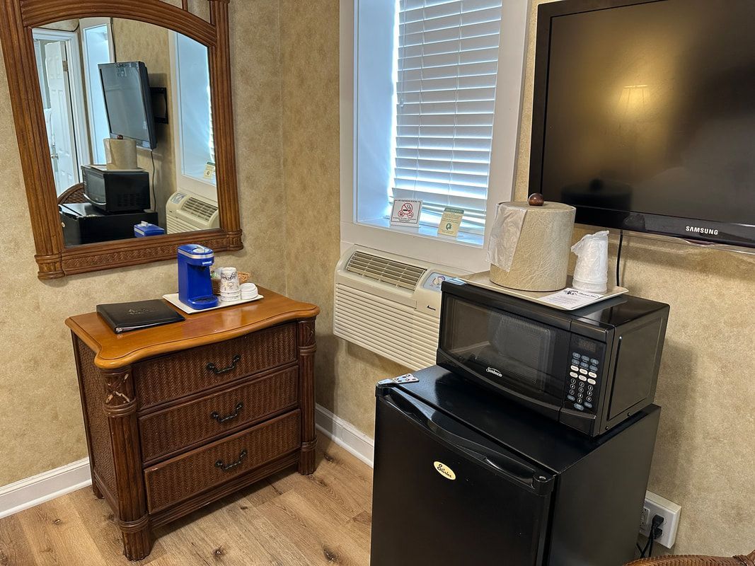 A hotel room with a dresser , microwave , refrigerator and television.