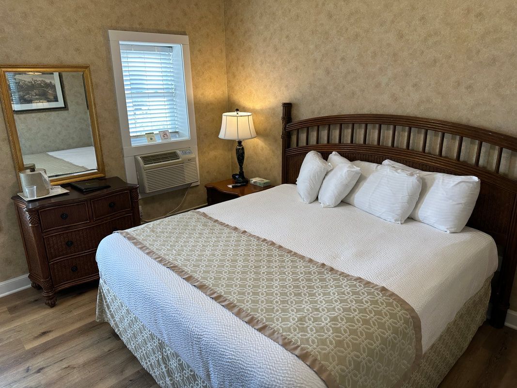 A bedroom with a king size bed , dresser , lamp and mirror.