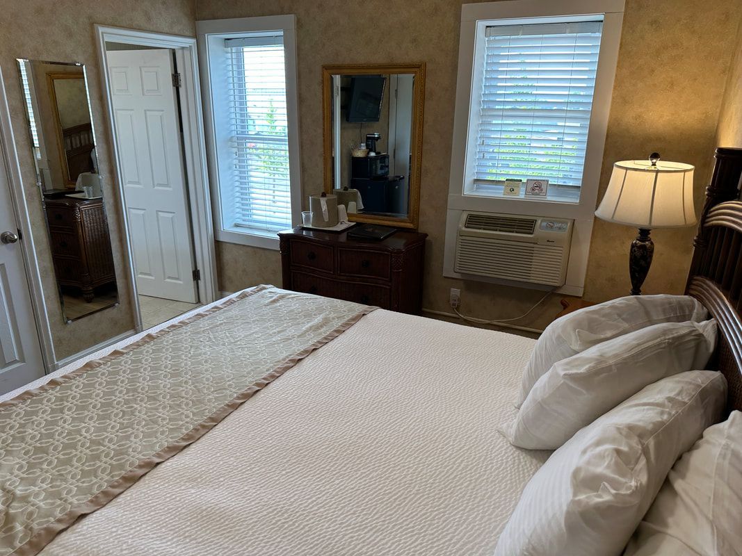 A bedroom with a king size bed , dresser , lamp , mirror and window.