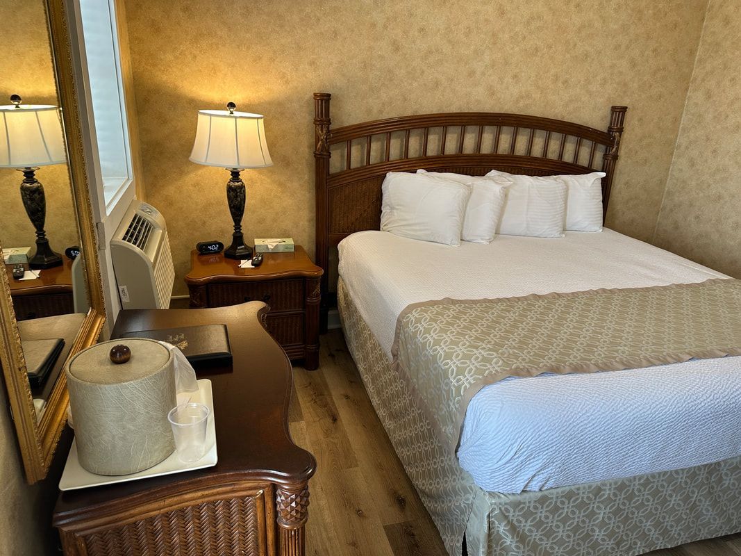 A hotel room with a bed , nightstand , mirror and dresser.