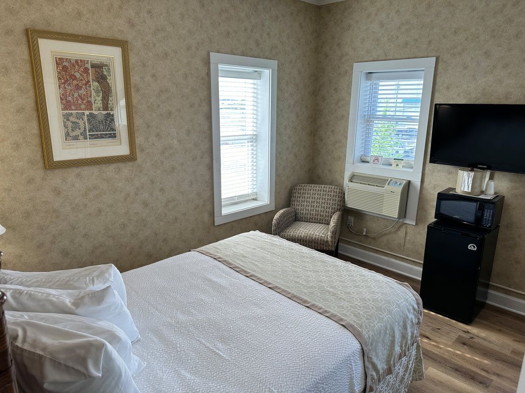 A hotel room with a bed , chair , television and refrigerator.