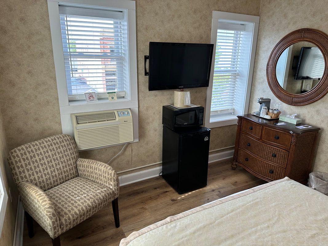 A bedroom with a bed , chair , television , dresser and mirror.
