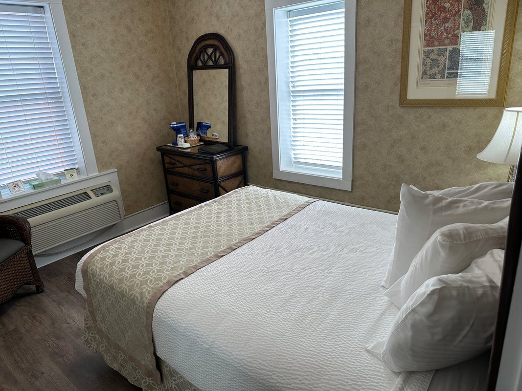 A bedroom with a bed , dresser , mirror and two windows.