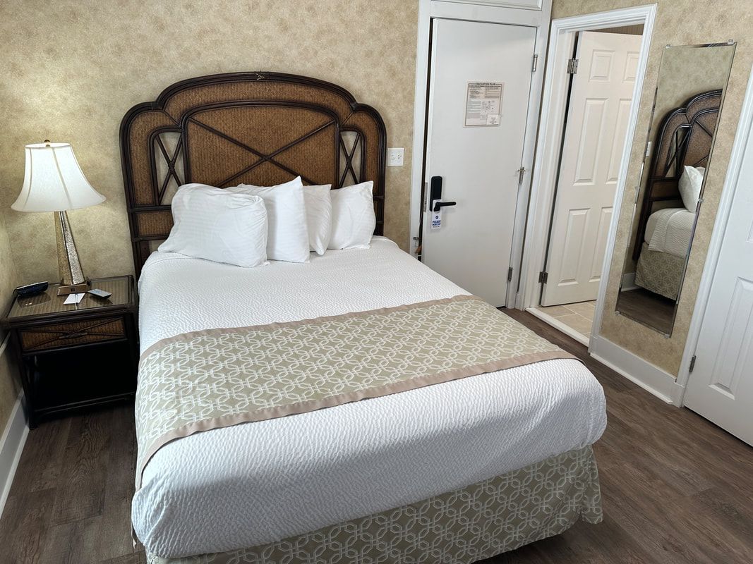 A hotel room with a king size bed , nightstand , lamp and mirror.